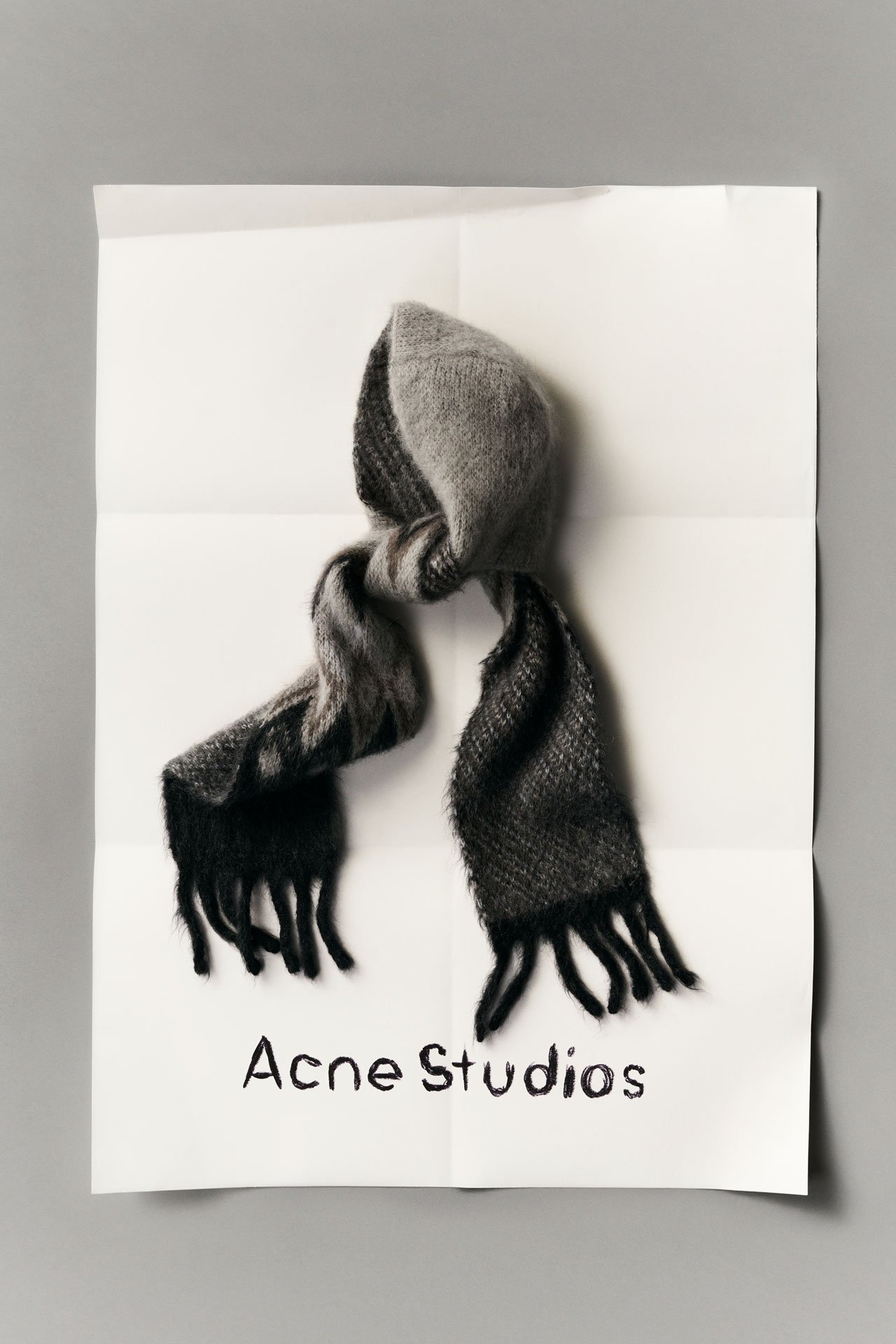 Acne Studios FW25 Gift Guide collection, a grey-black wool scarf on a peace of paper with Acne Studios logo.