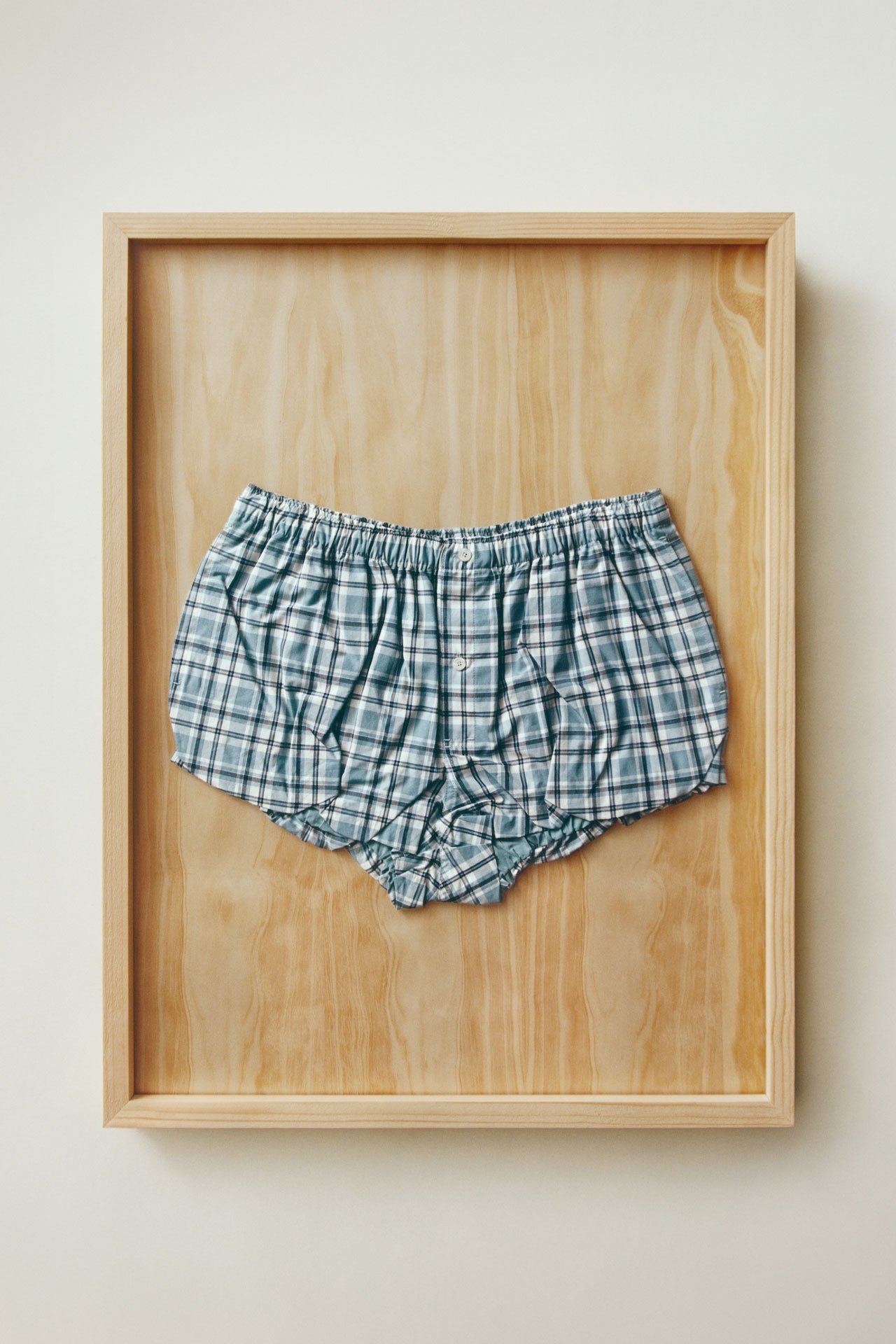 Acne Studios blue checked shorts presented on a wooden tray.