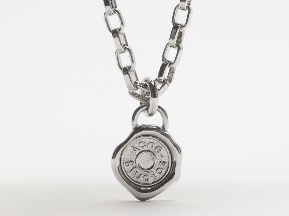 A close-up of the Acne Studios silver necklace with logo details.