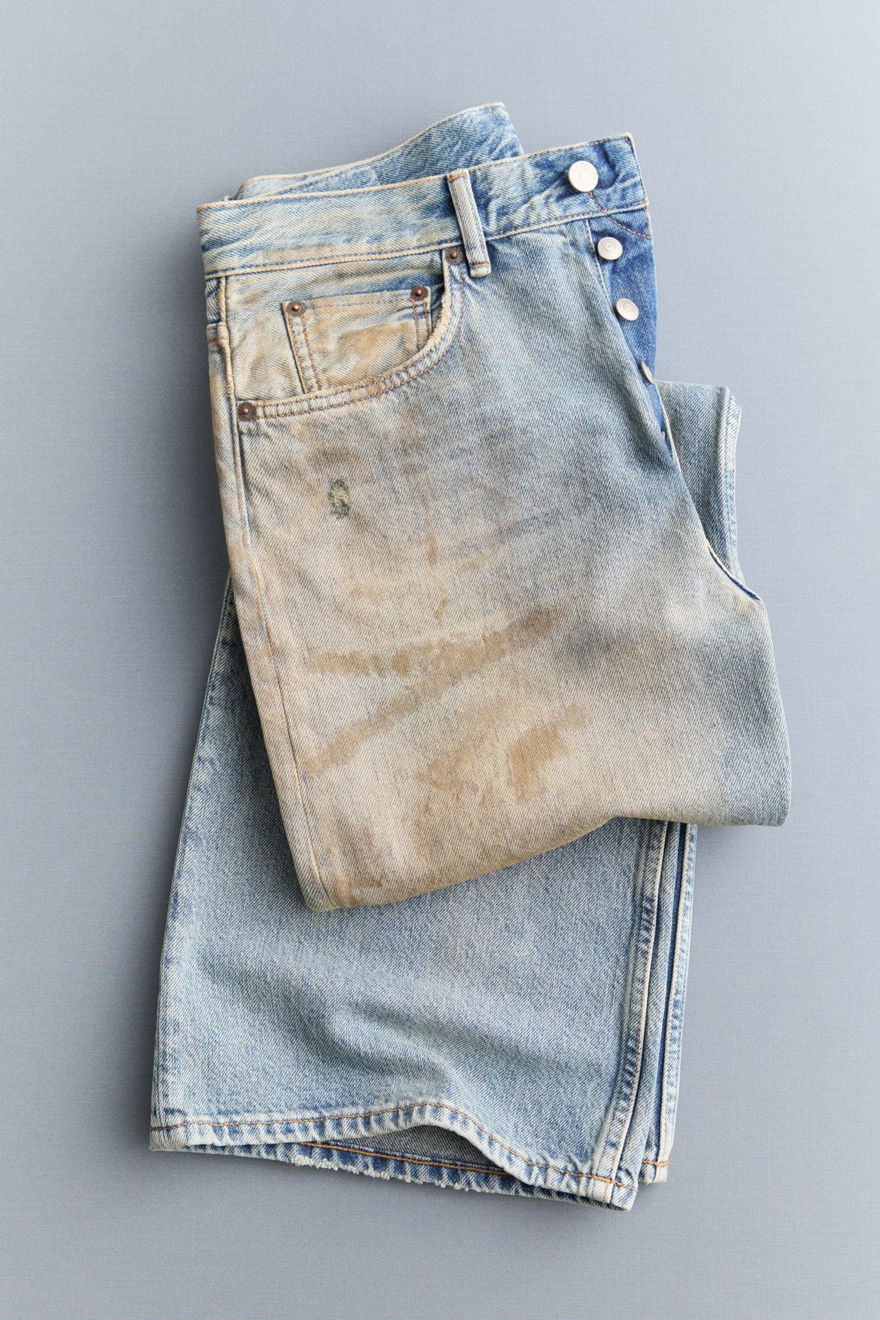 Acne Studios Man 1996M light blue ripped straight jeans, grey-blue knitted sweater, black leather Camero bag and brown leather belt.