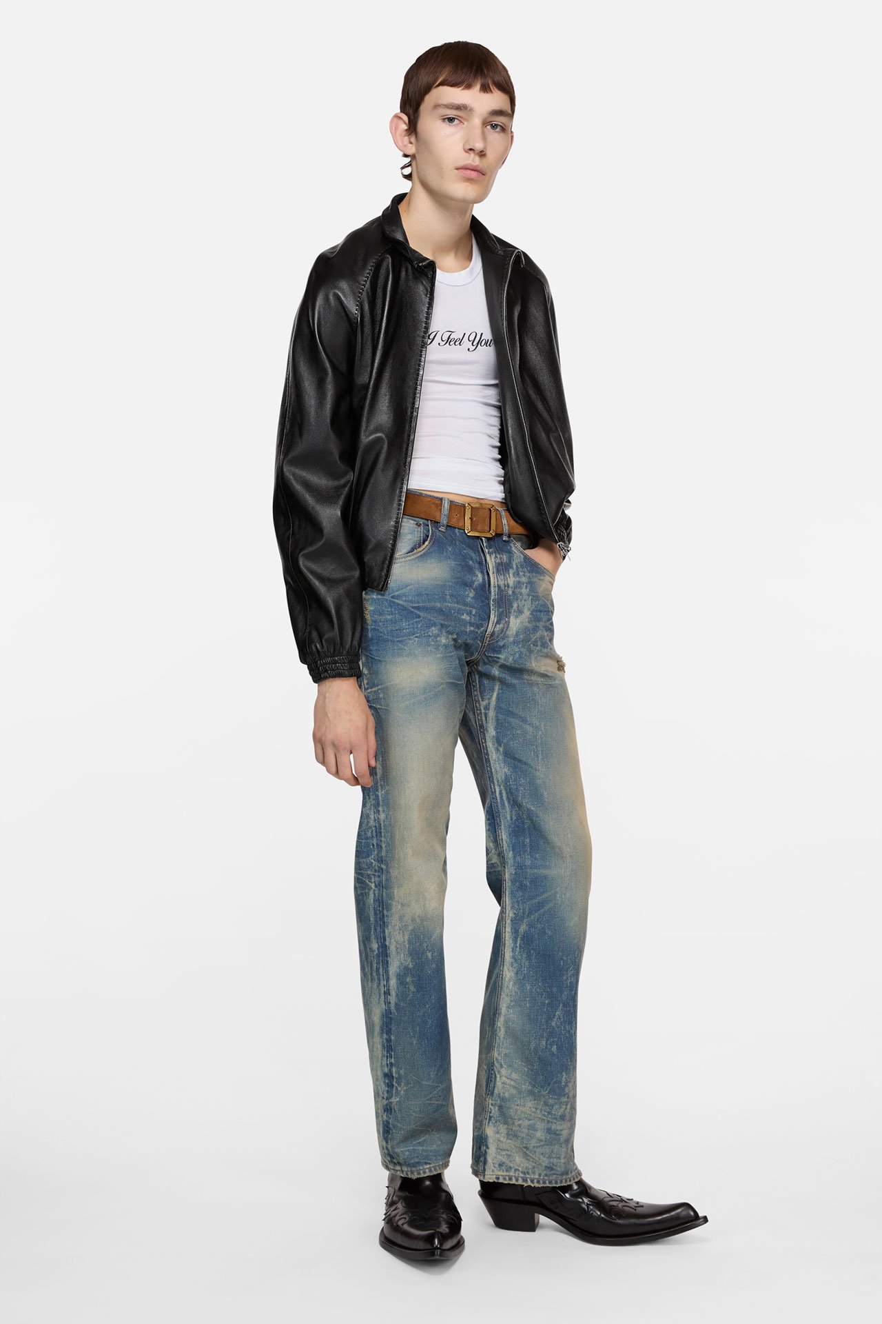 A male model wearing a white shirt, black leather jacket, blue jeans and black leather boots.