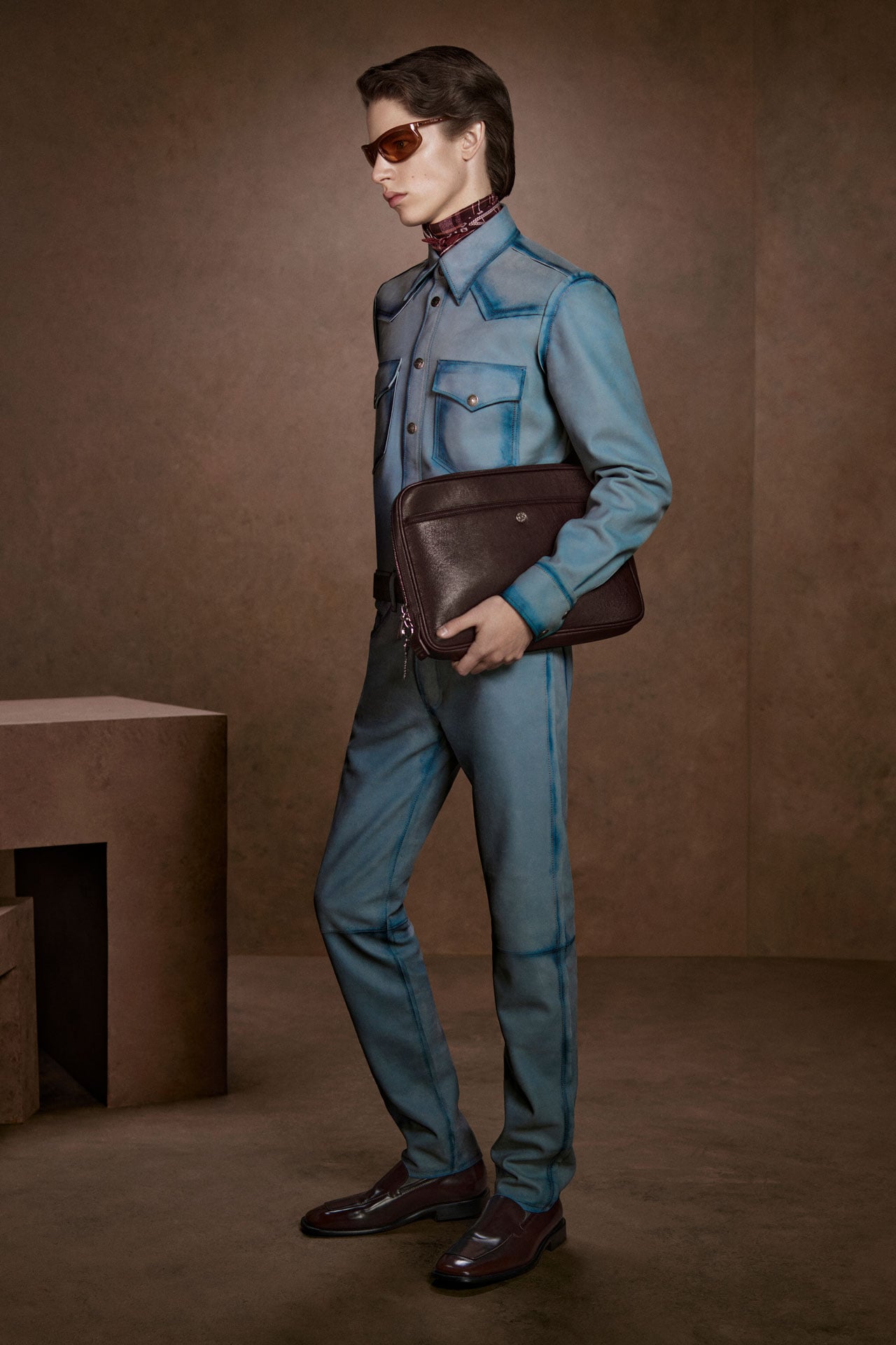 Acne Studios matching set of light blue jeans and denim shirt, and a brown leather laptop case.
