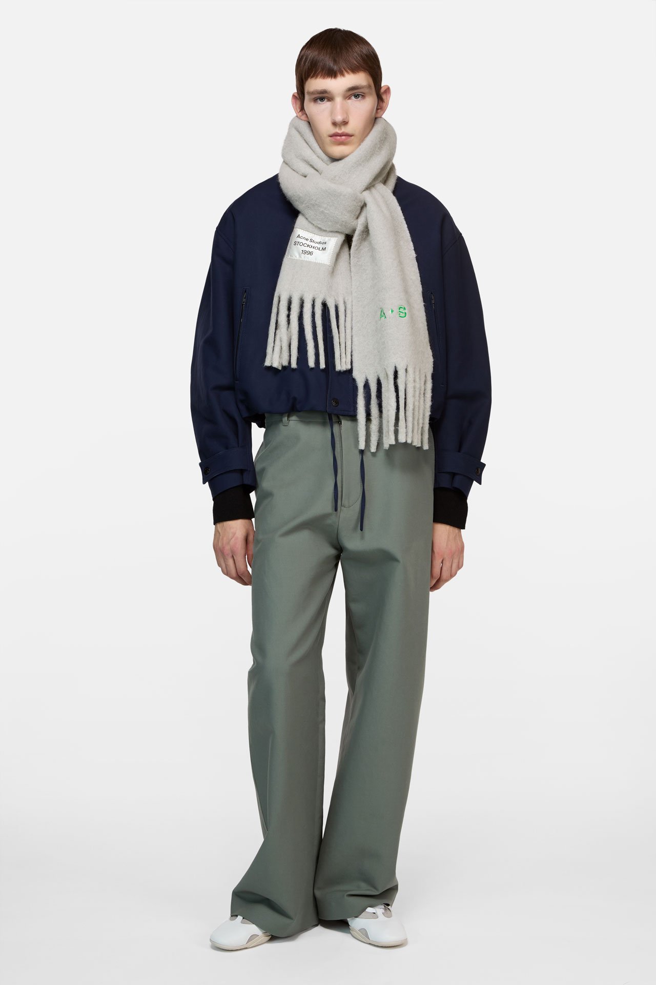 Male model wearing an Acne Studios 1996 grey melange alpaca scarf in grey, blue bomber jacket, grey pants and white sneakers.
