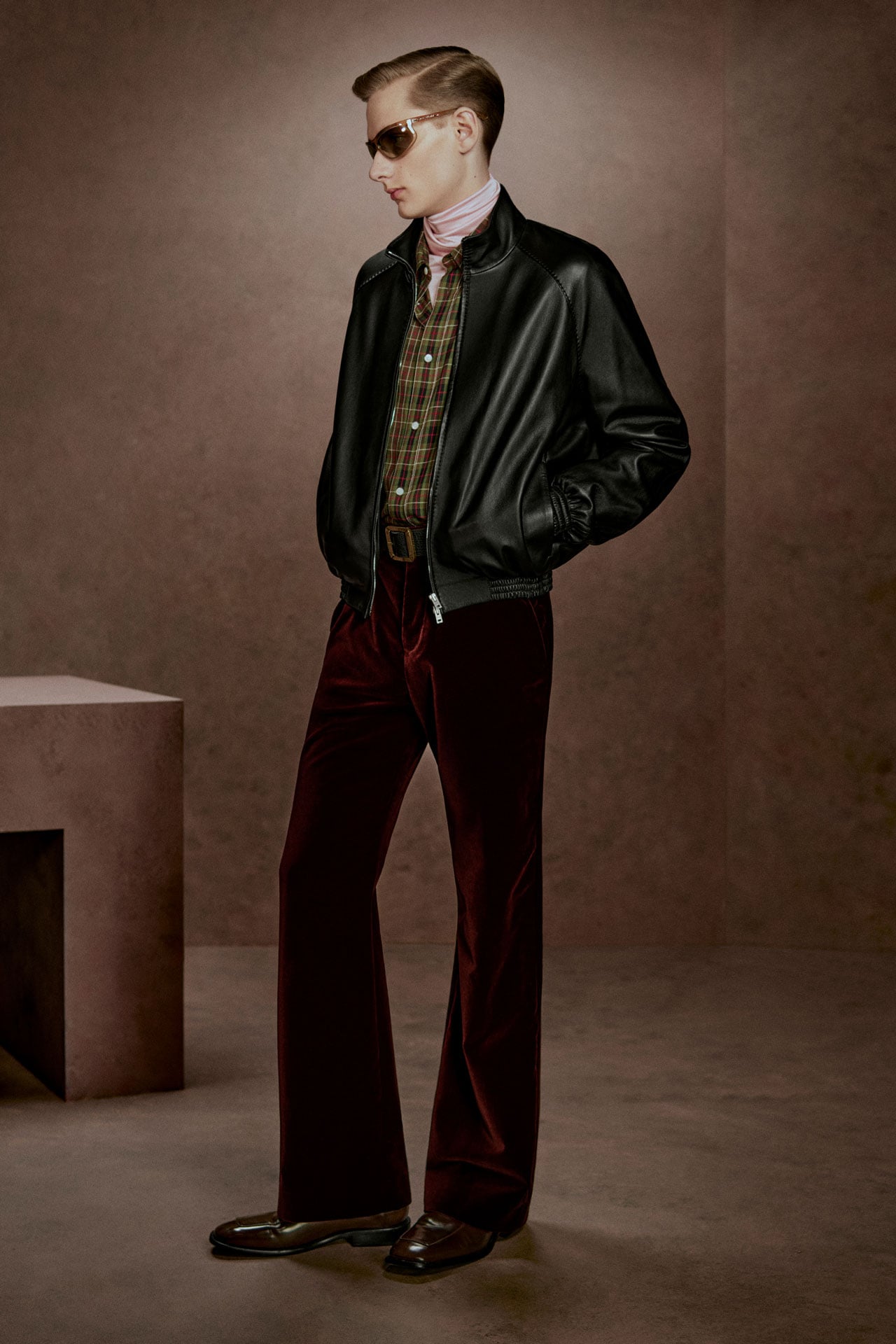 Acne Studios black leather bomber jacket, dark red velvet trousers, brown checked shirt and dark sunglasses.