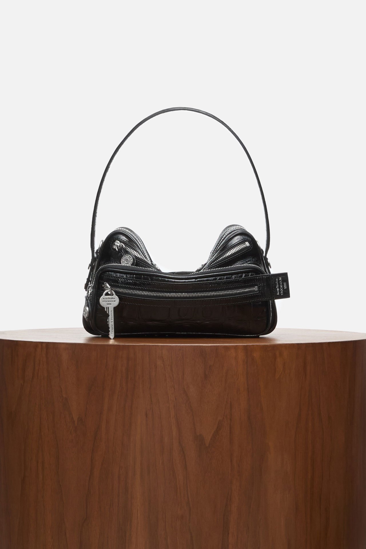 A creative showcase of a black leather crocs Camero bag on a wooden pedestral.