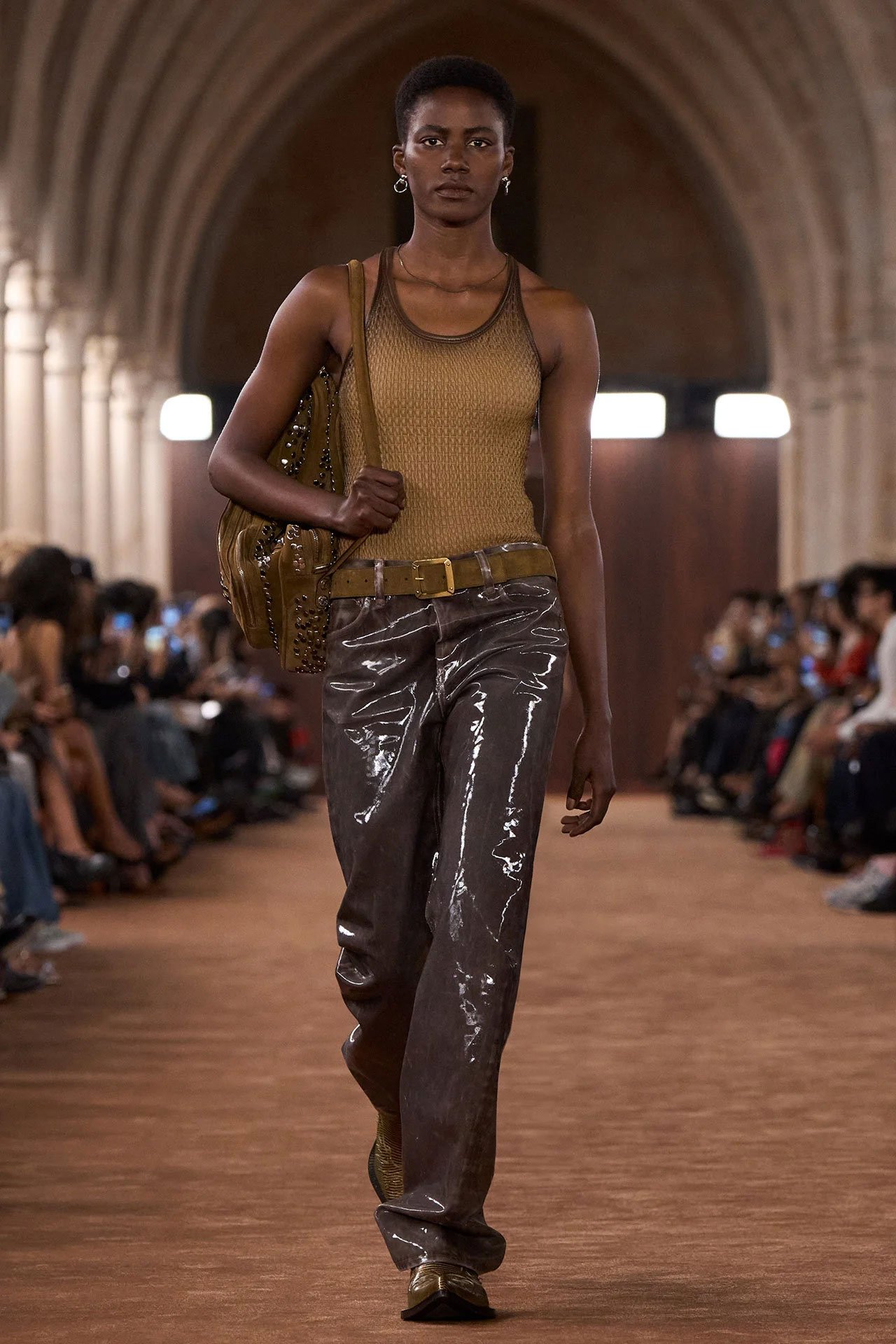 Acne Studios SS26 Runway - a female model wearing a sand-colored tanktop, brown leather pants and a brown suede Camero bag.