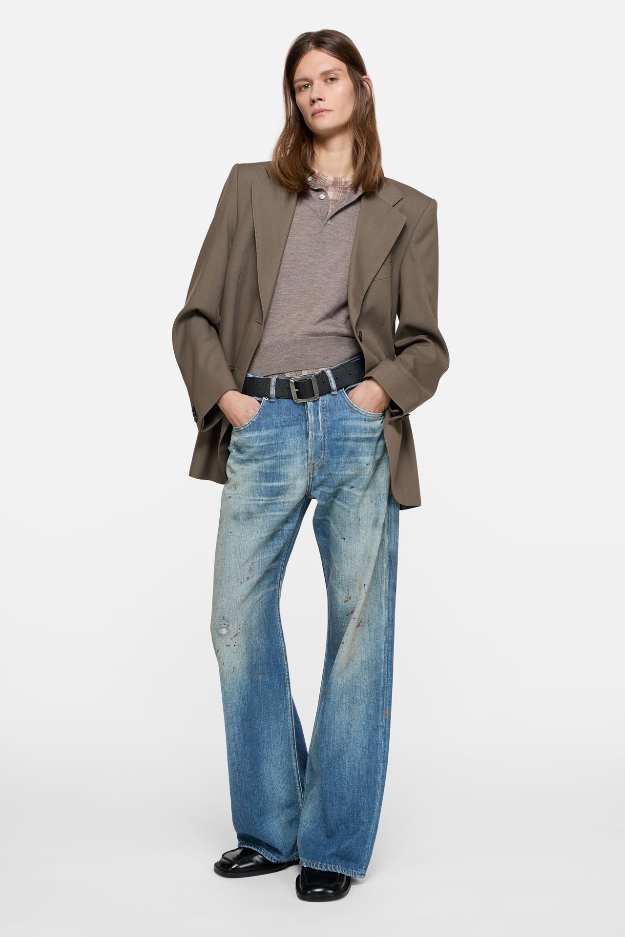 A female model wearing a mid-blue jeans Acne Studios, beige suit jacket and beige shirt.