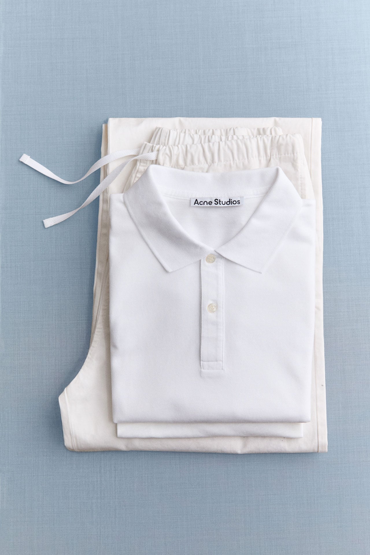 Acne Studios White on white collection white polo t-shirt folded on white pants.