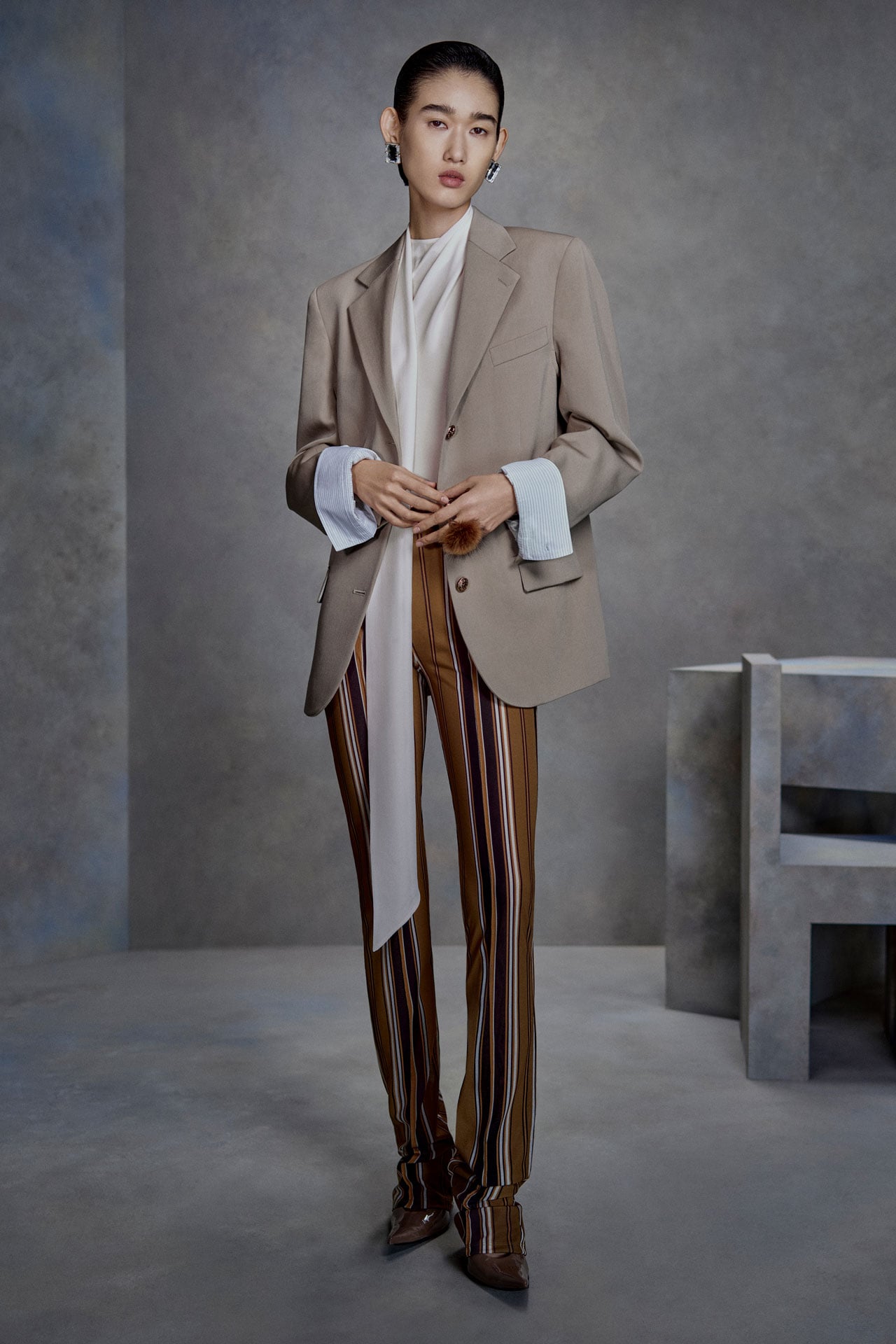 Acne Studios Womenswear taupe tailored jacket, white silk top, brown striped pants.