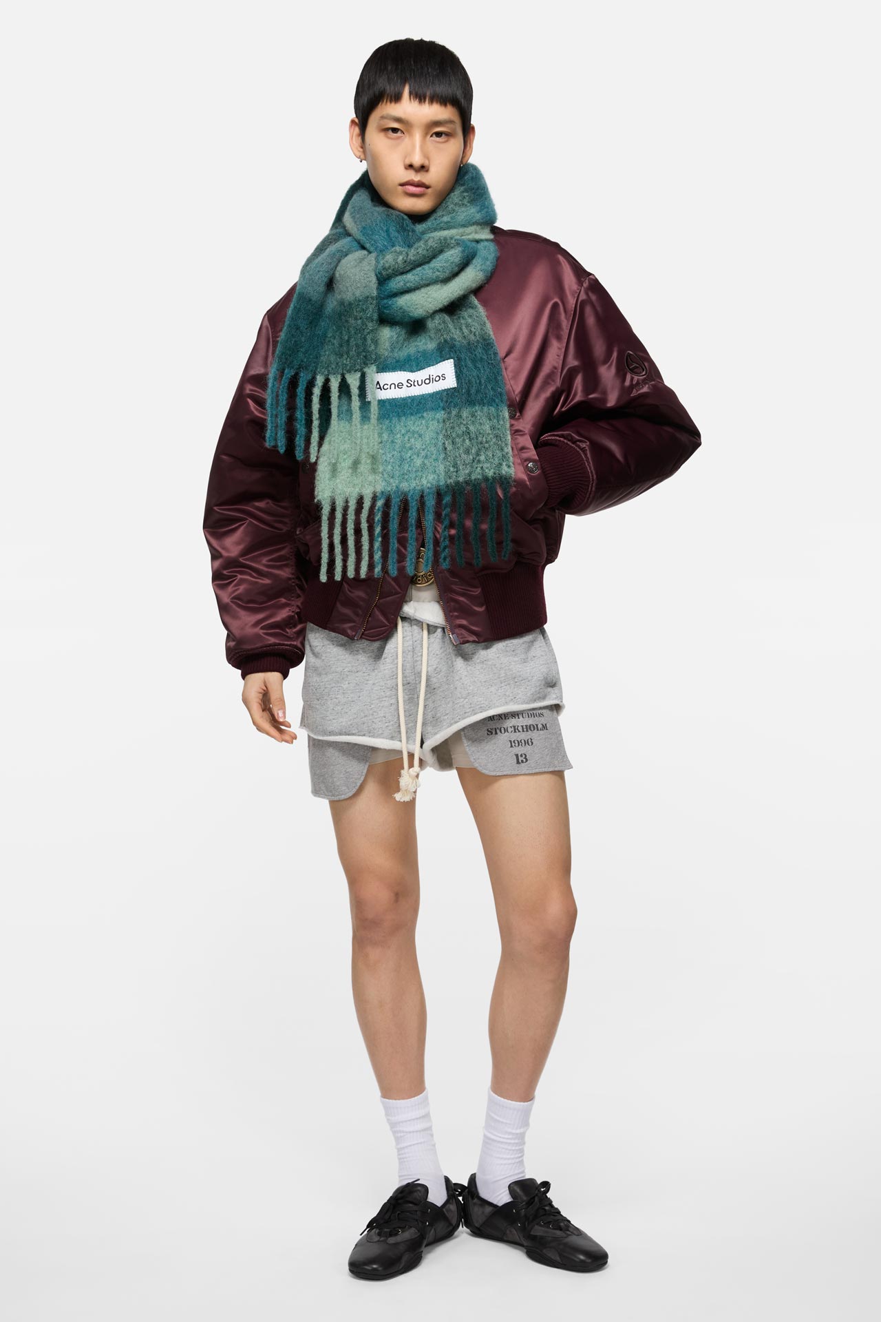 Male model wearing Vally mohair mix teal checked scarf by Acne Studios, vine-red bomber jacket and grey shorts.