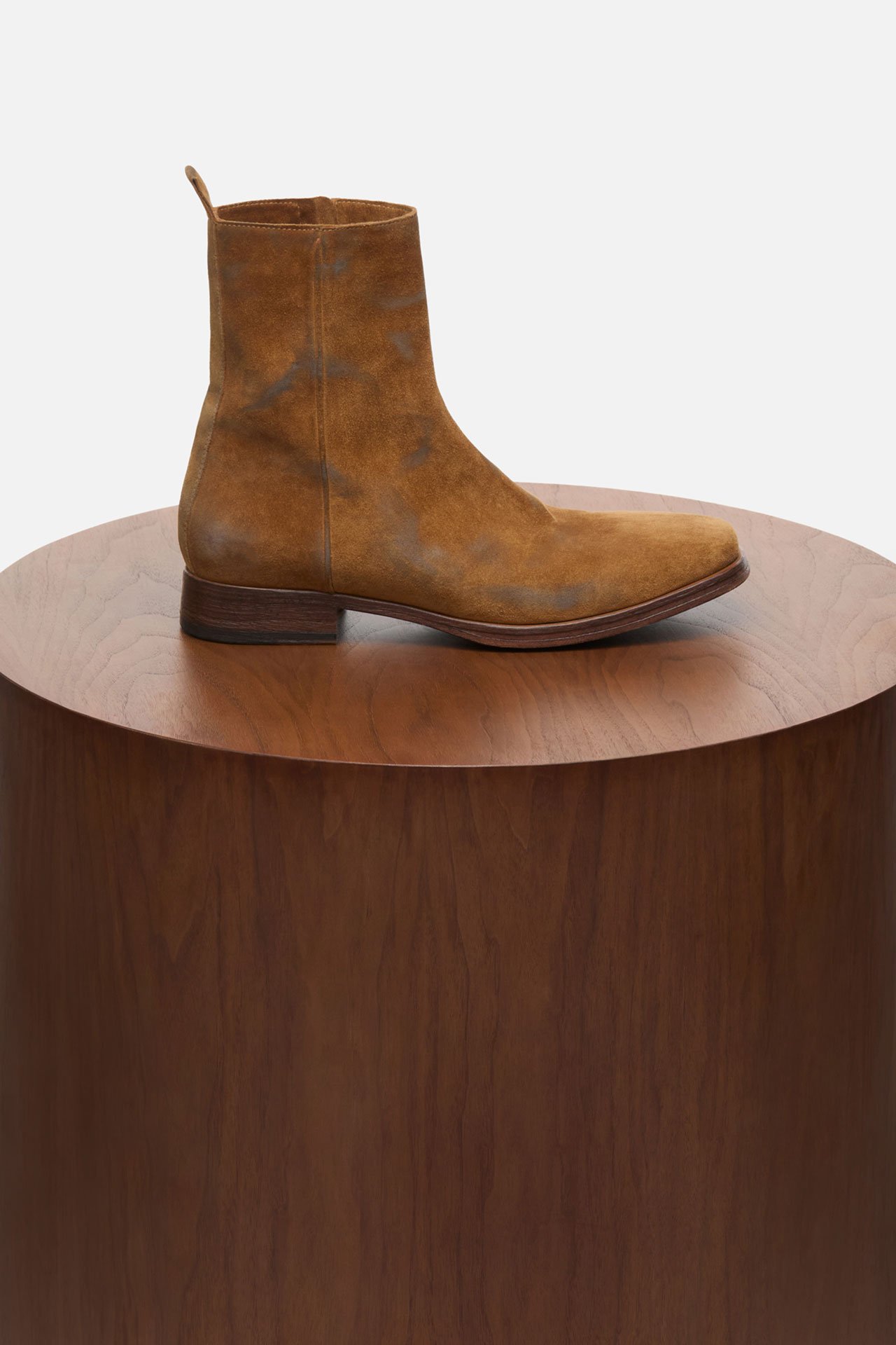 A creative showcase of mens beige suede boots on a wooden pedestral.