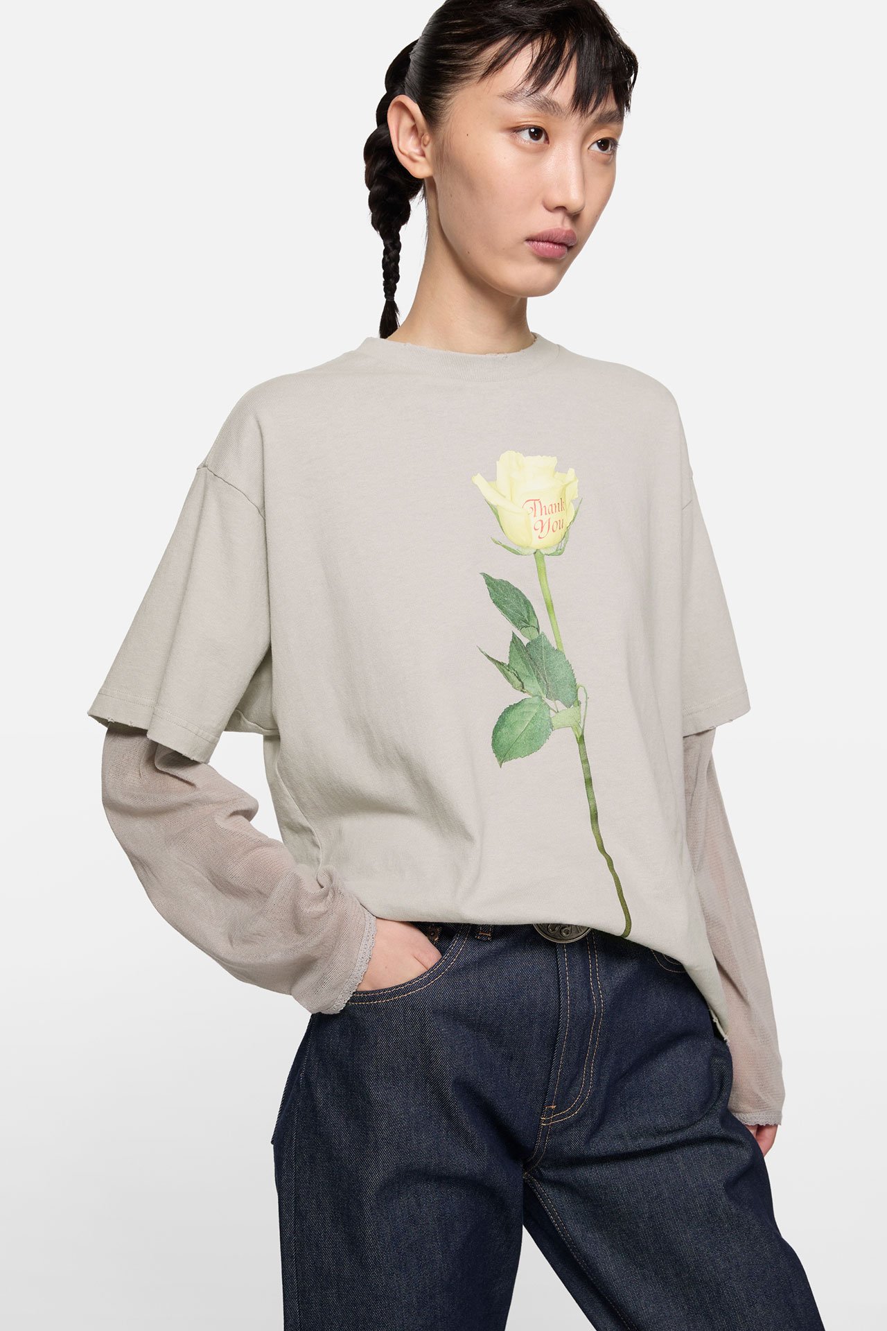 Female model wearing and Acne Studios taupe t-shirt with a white rose print, and a pair of dark wash jeans.