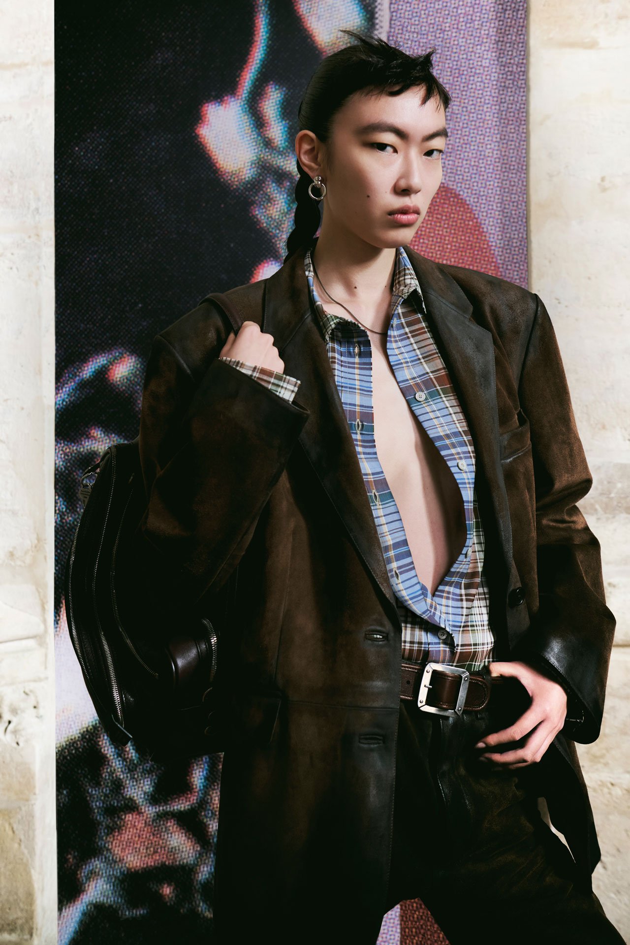 Acne Studios SS26 Runway - a female model wearing blue checked open shirt, leather trousers, brown leather belt, brown oversized leather jacket and holding a leather Camero bag.
