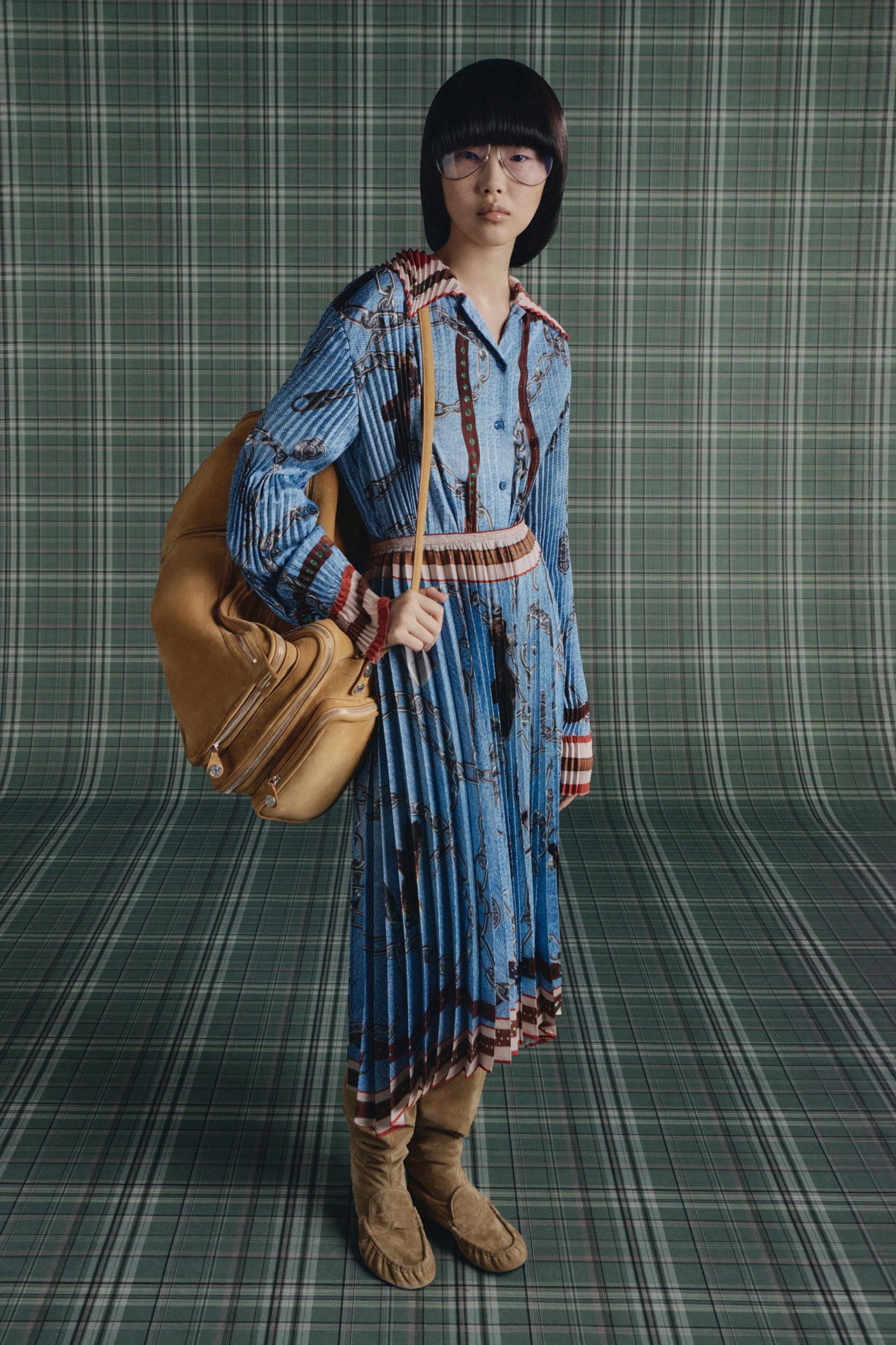 Black short bob-haired female model wearing glasses, Acne Studios blue printed shirt and skirt, beige boots and a big beige Camero bag.