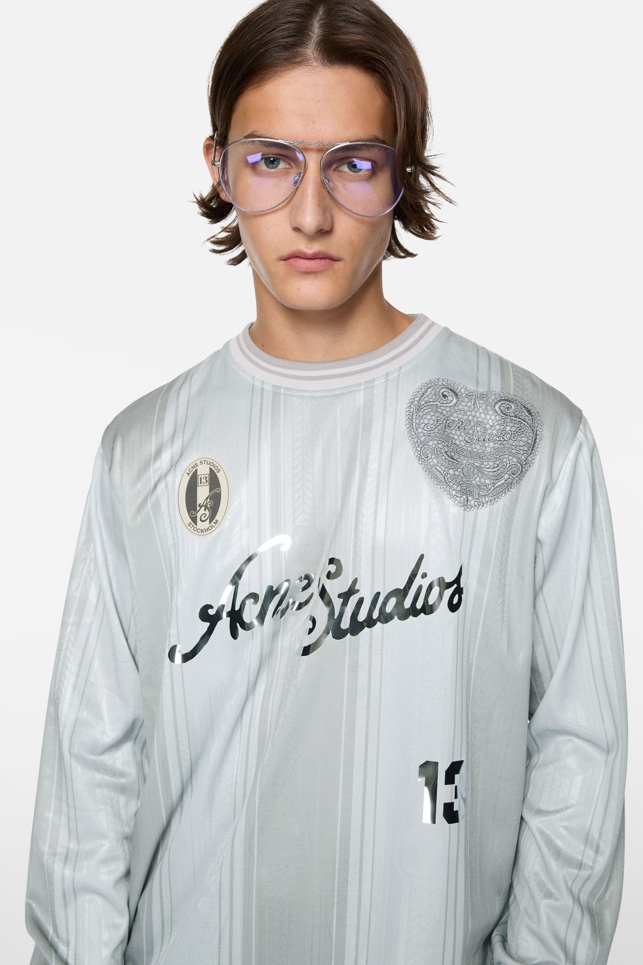 A male model wearing an Acne Studios light blue football shirt-like long-sleeved shirt.