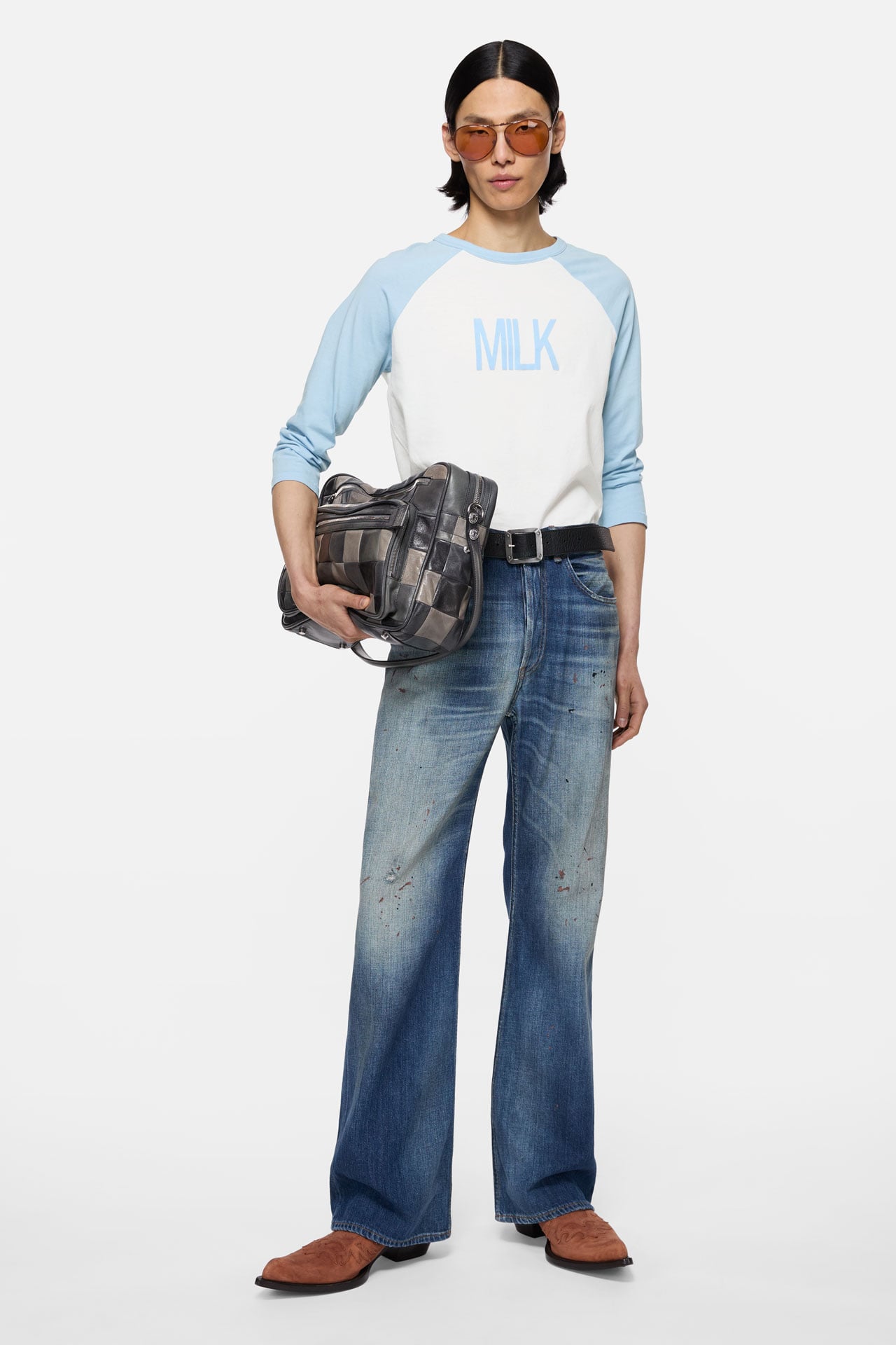 Acne Studios Menswear white long-sleeve t-shirt with blue arms, blue jeans and holding a grey leather Camero bag.