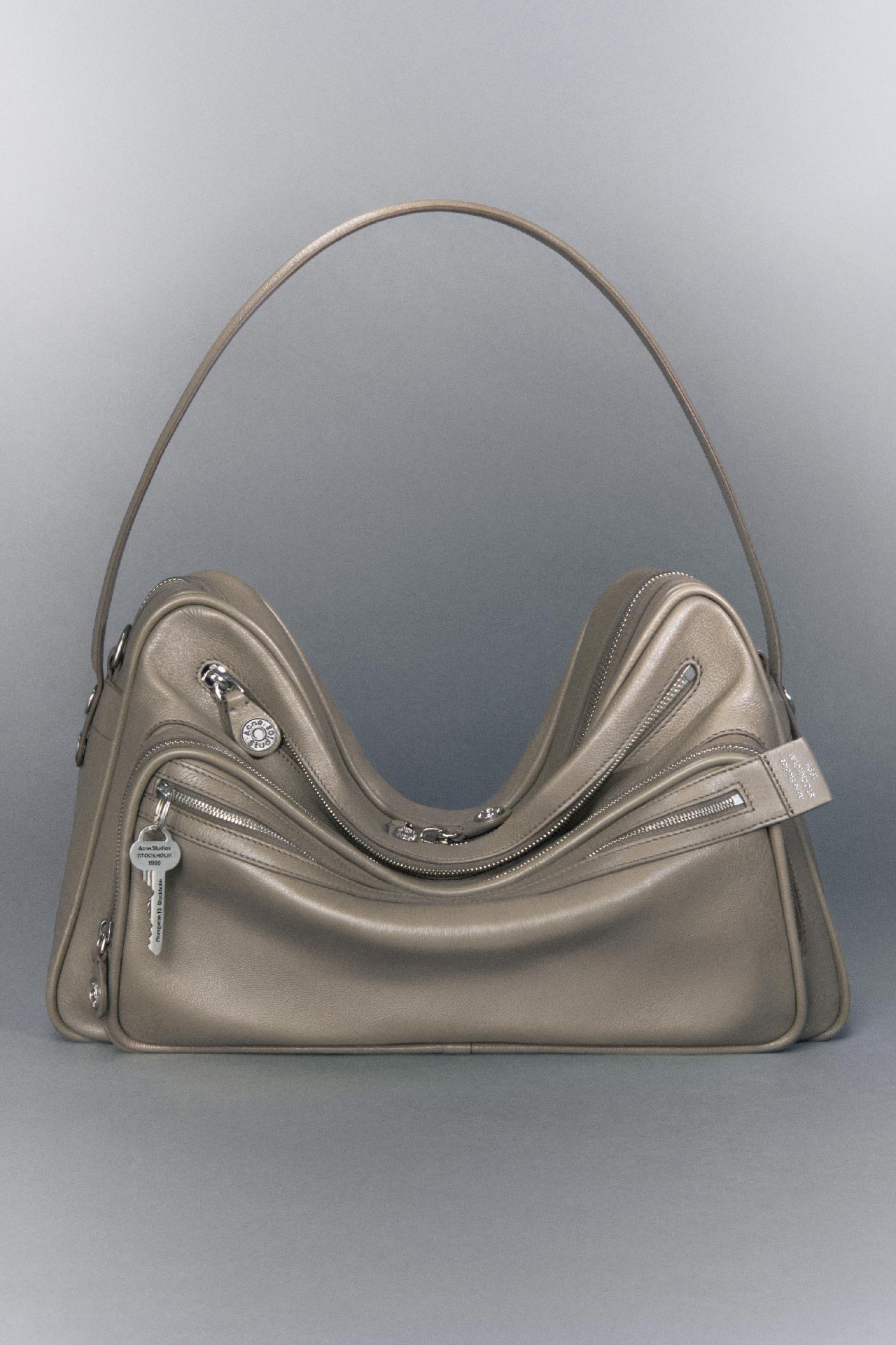 Acne Studios Camero Camera shoulder bag in taupe beige with grey background.
