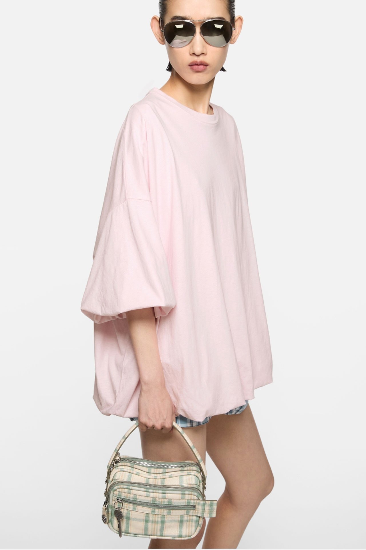 Female model wearing and Acne Studios babypink oversized t-shirt and holding a beige-green checked mini leather Camero bag.