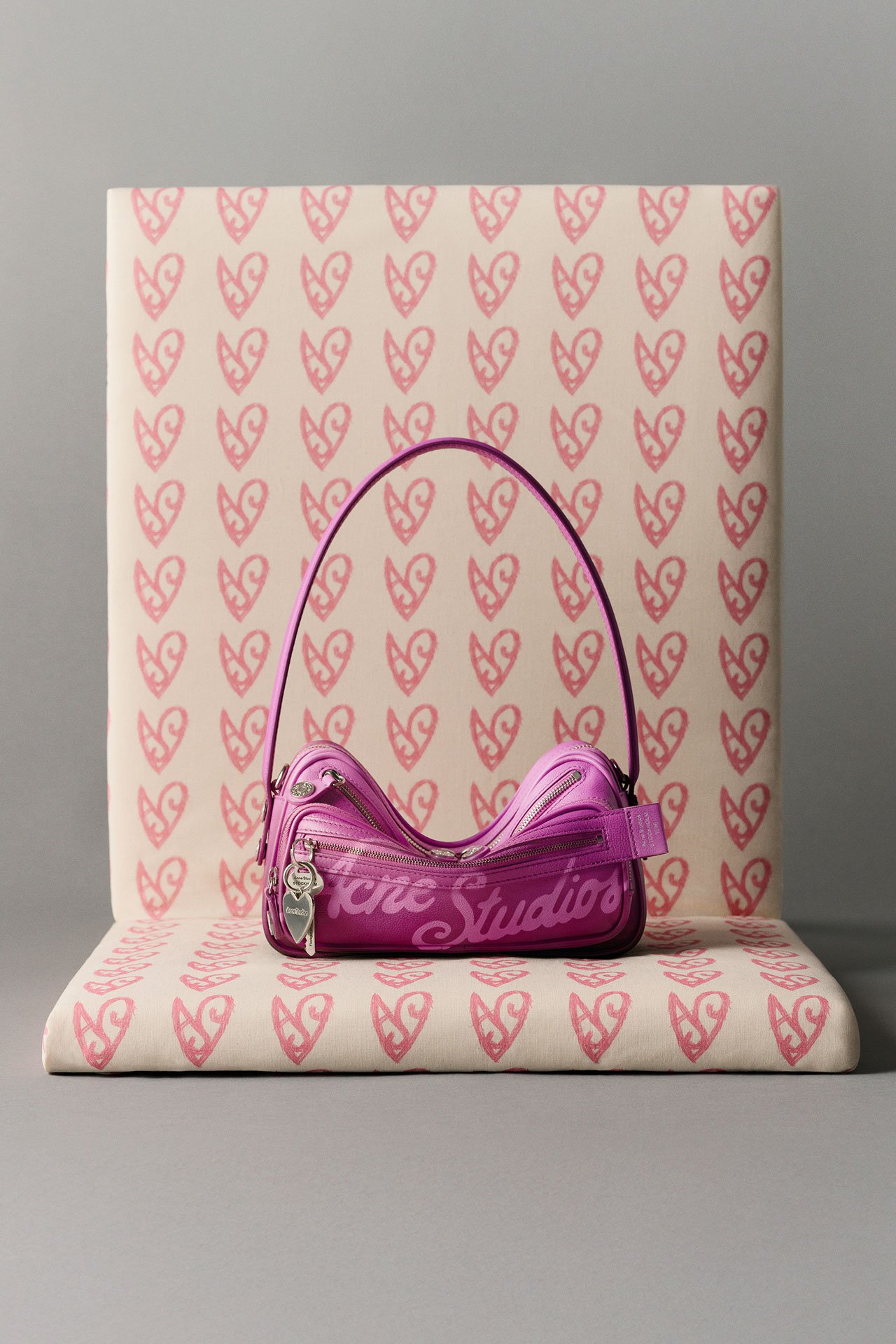 Acne Studios FW25 Gift Guide collection, a pink Camero bag with a logo on it, in front of a signature heart-patterned giftwrap background.